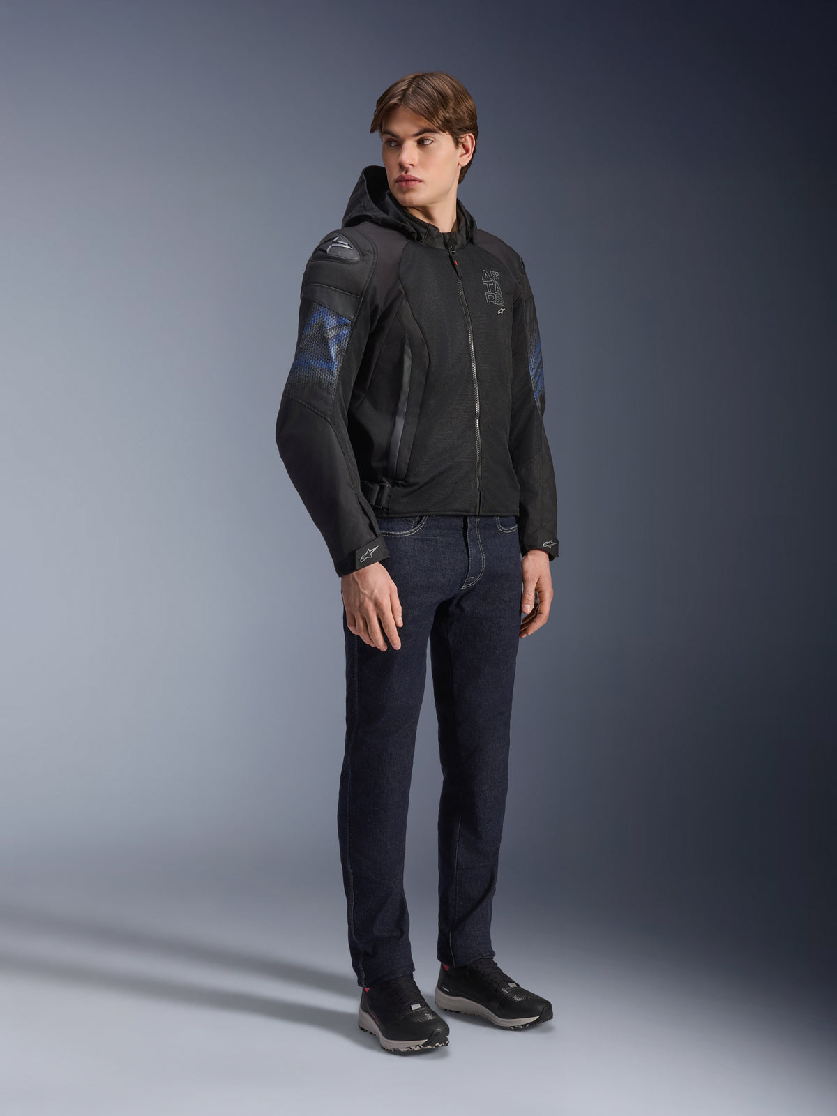 Veste Alpinestars Zaca Air Venom WP, veste de moto en textile noir et bleu électrique, portée par un mannequin avec un jean foncé et des baskets noires, dotée d'une capuche amovible, de panneaux de ventilation en maille et de sliders d'épaule DFS Lite, équipement de conduite sportif toutes saisons.