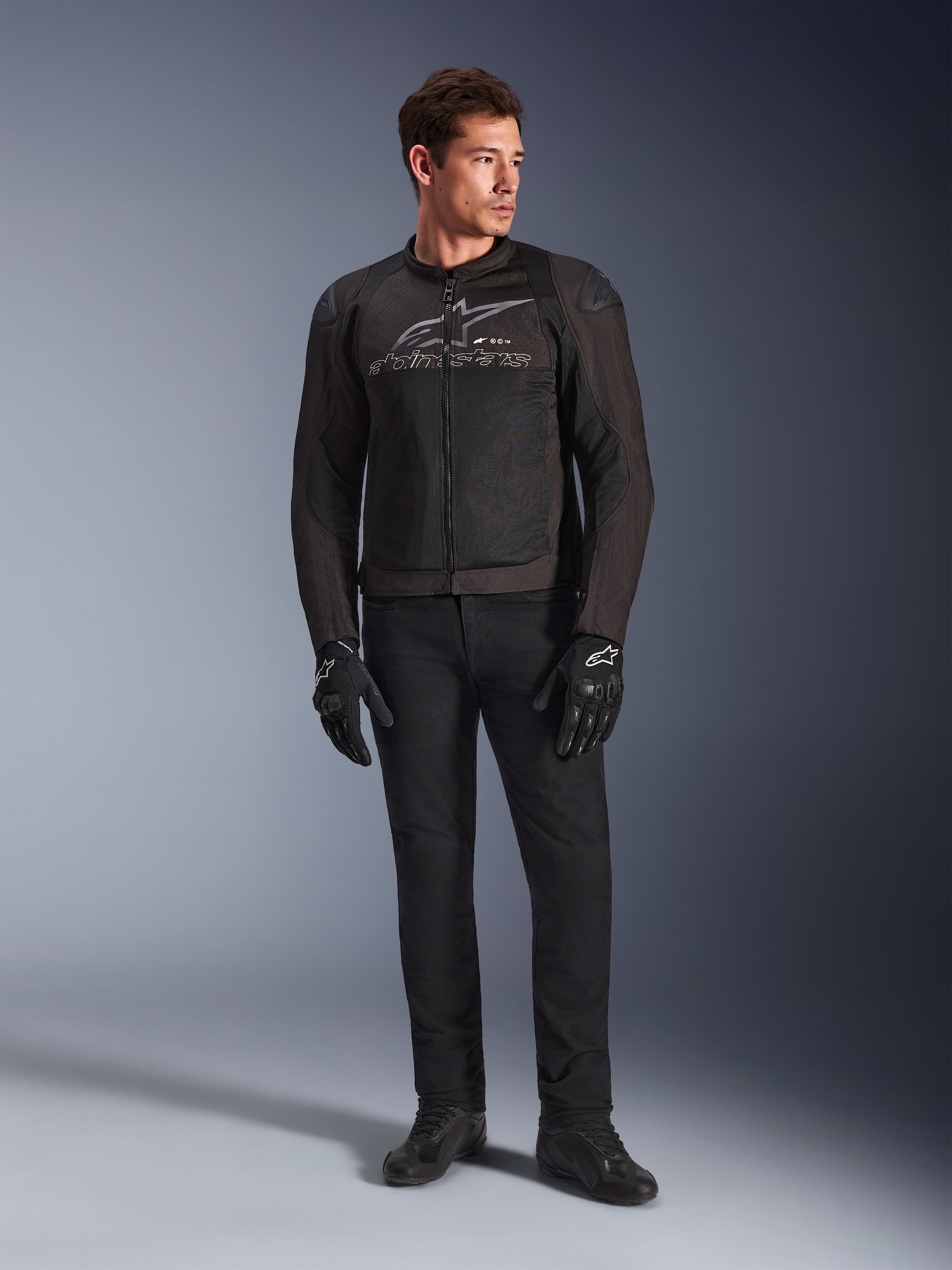 Mannequin homme portant la veste de moto Alpinestars SMX Air, coloris Black Anthracite, avec panneaux en maille ventilée et logo gris sur la poitrine, associée à un pantalon noir et des gants de protection, studio avec fond en dégradé