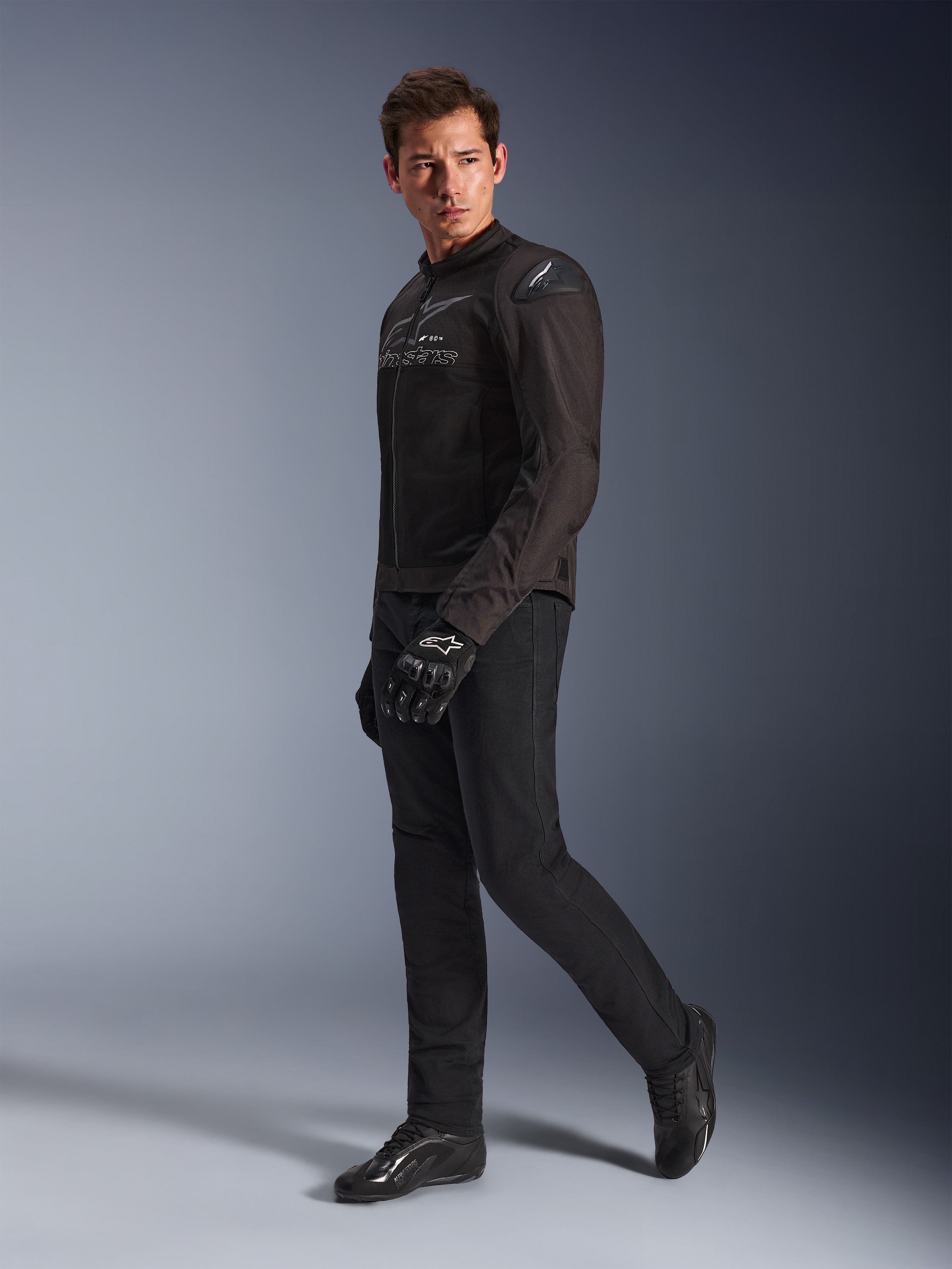 Veste Alpinestars SMX Air en Noir Anthracite, portée par un mannequin avec pantalon de moto, gants et chaussures noirs assortis, cliché studio en pied, équipement moto sport de performance avec maille technique et sliders d'épaule