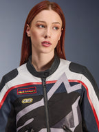 Veste femme Alpinestars Idles, gros plan d'un mannequin aux cheveux roux, coloris blanc cassé, rouge et noir, design de course d'inspiration vintage avec écussons et graphismes d'étoiles géométriques grises, équipement de moto urbain
