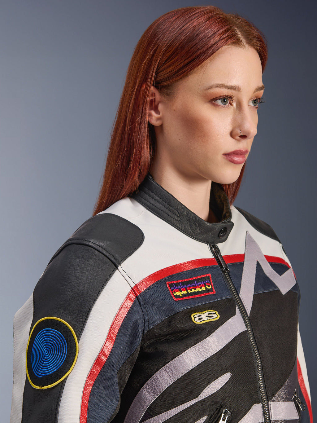 Veste Alpinestars Idles pour femme, blanc cassé, rouge flamme et noir, avec des écussons de course d'inspiration vintage et un logo enveloppant, conception en textile et cuir, style moto urbain portée par un mannequin