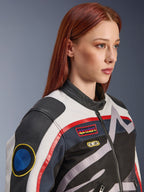 Veste Alpinestars Idles pour femme, blanc cassé, rouge flamme et noir, avec des écussons de course d'inspiration vintage et un logo enveloppant, conception en textile et cuir, style moto urbain portée par un mannequin