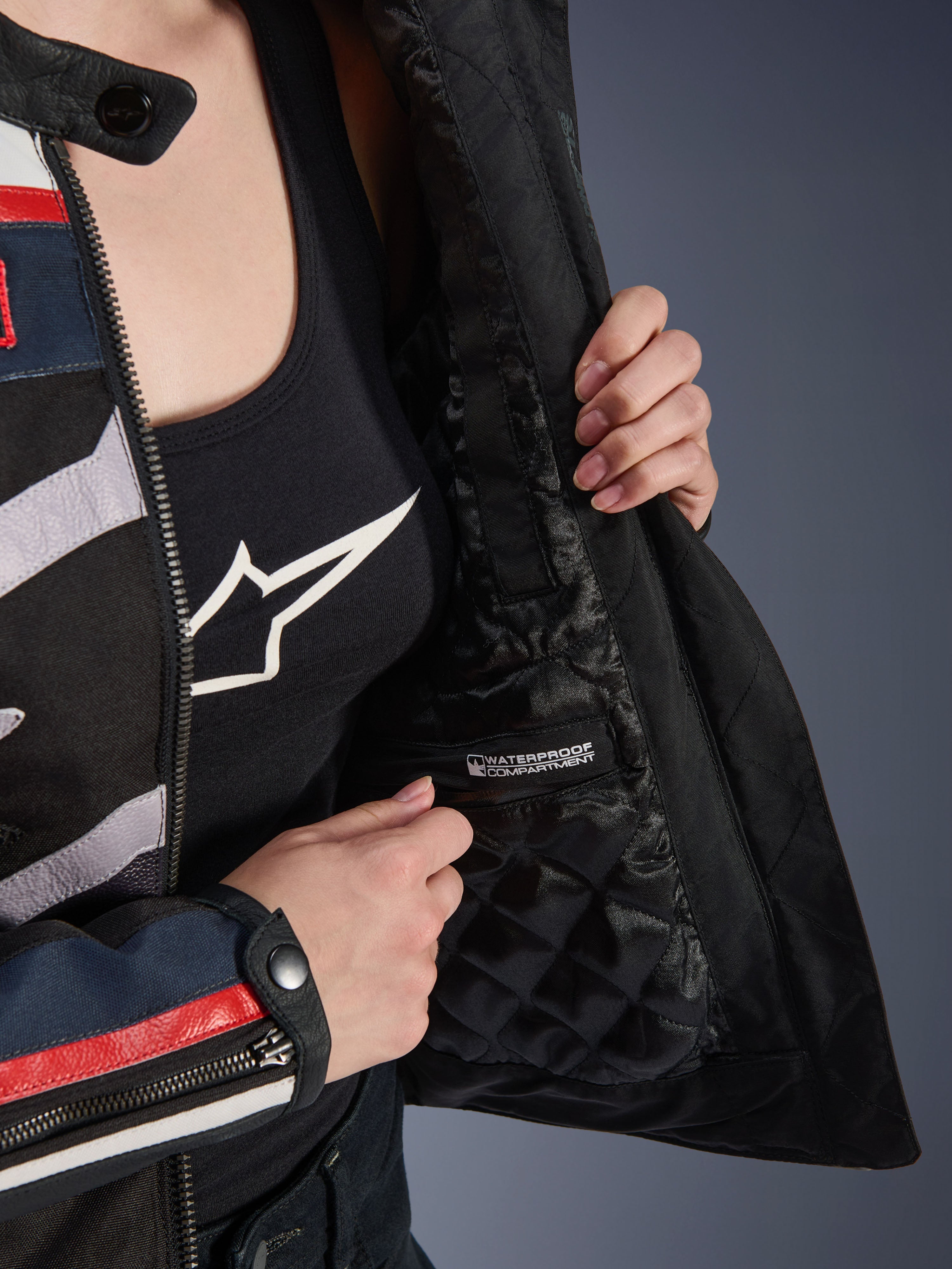 Veste Idles Femme Alpinestars, détail de l'intérieur montrant la doublure matelassée noire et le compartiment étanche étiqueté, portée sur un débardeur noir à logo, équipement de moto fonctionnel pour femmes