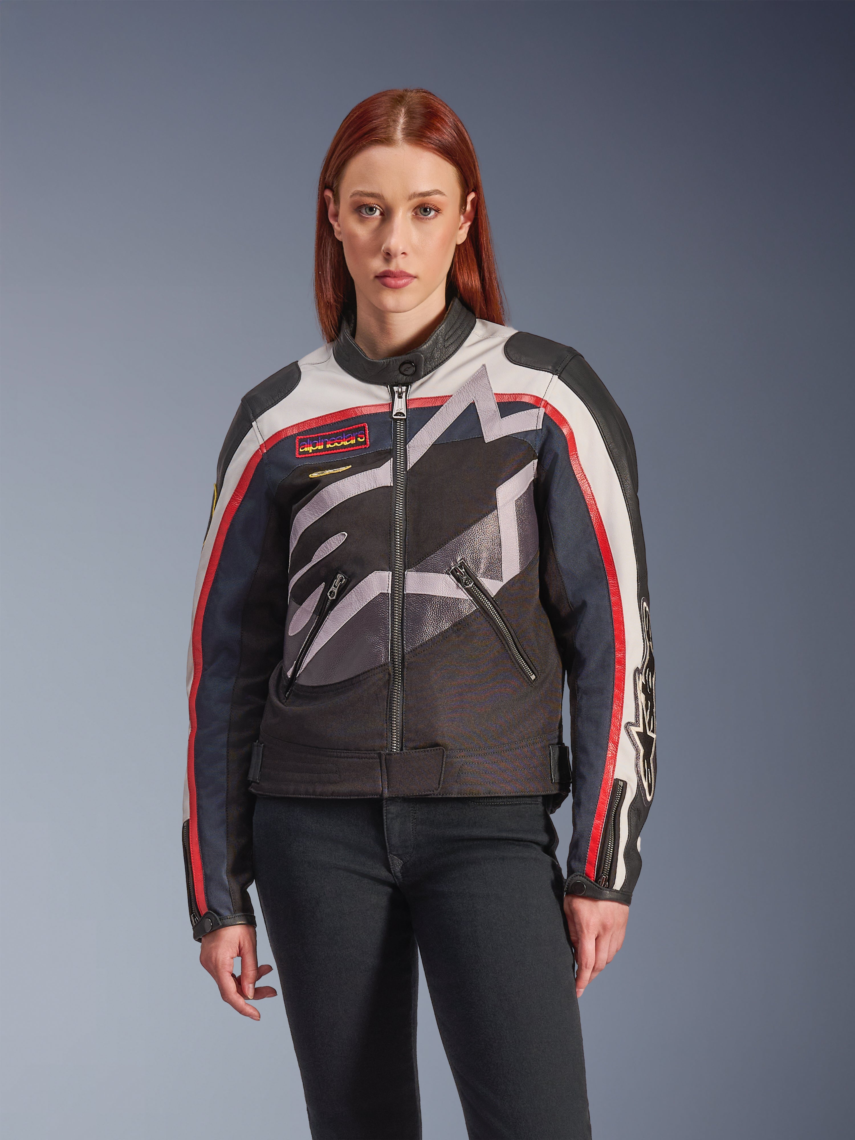 Veste Alpinestars Idles, veste de moto pour femme, blanc cassé, rouge flamme et noir, avec un grand logo étoilé stylisé, des écussons d'inspiration vintage sur la poitrine, un col montant, des poches zippées et des manches rayées, portée par un mannequin femme avec un jean foncé
