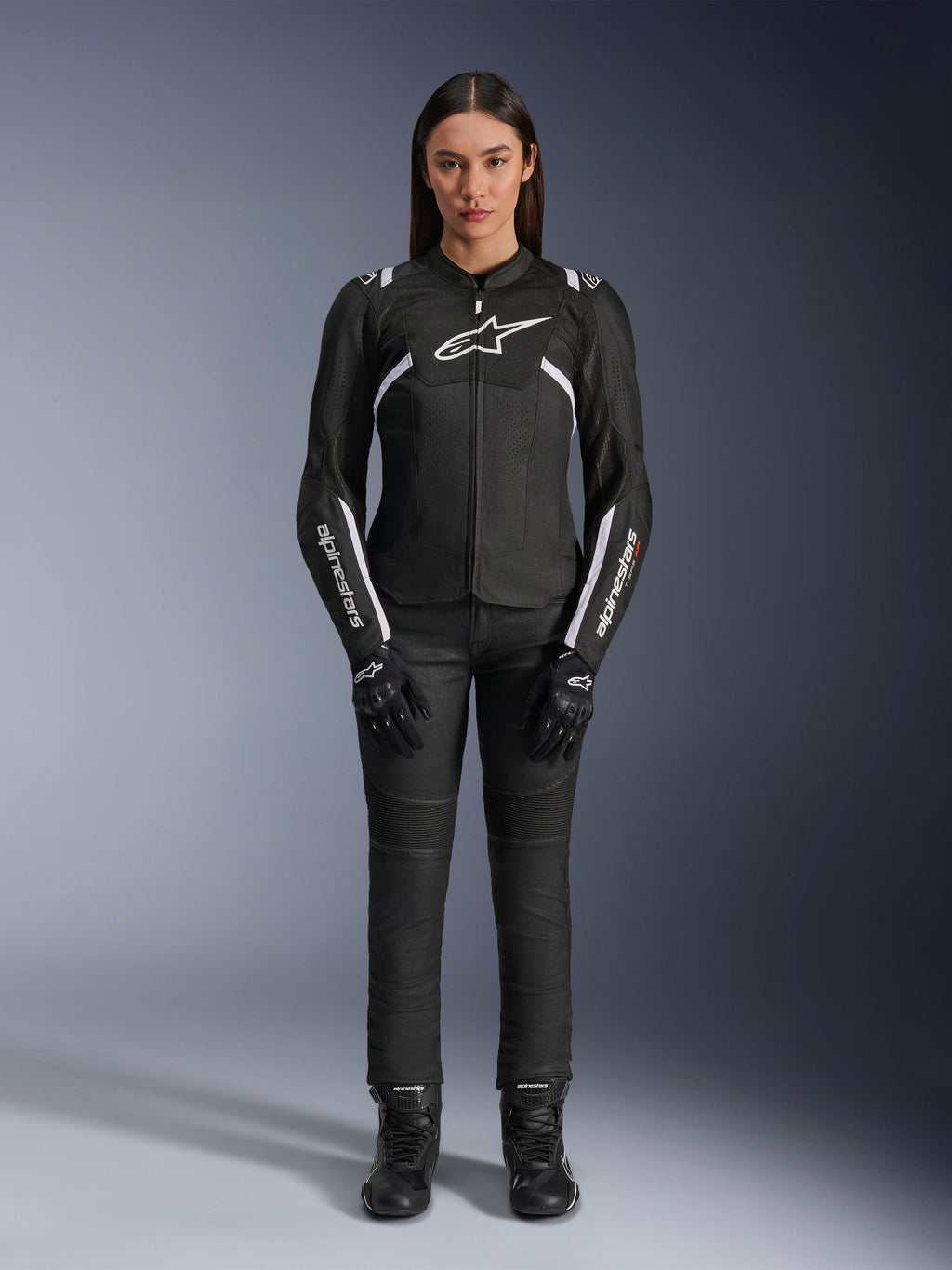 Veste Alpinestars Stella T-Sps Air V2, veste de moto pour femme, noir et blanc, avec panneaux en mesh et détails blancs, portée avec un pantalon, des gants et des bottes noirs, coupe athlétique pour une conduite urbaine