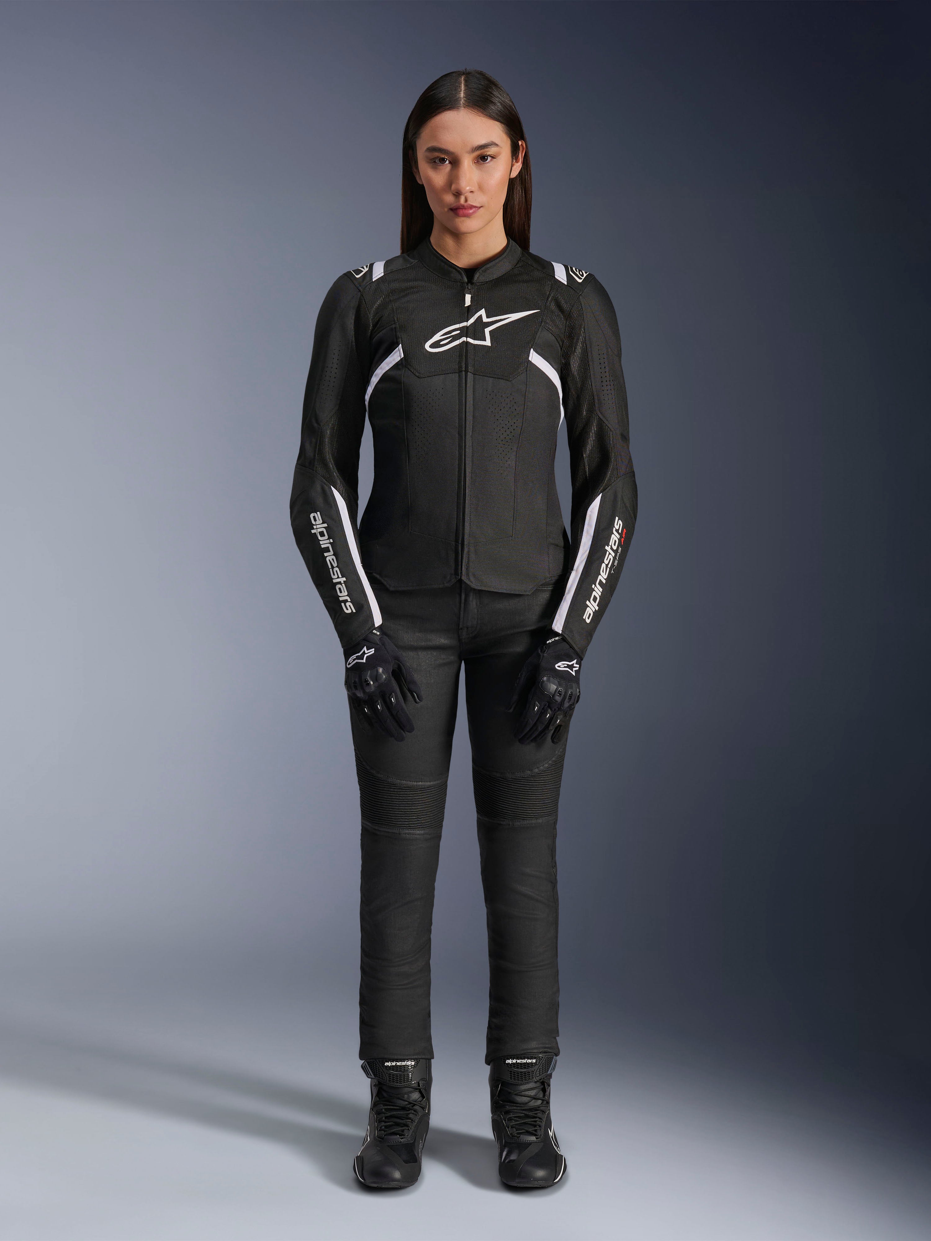 Veste Alpinestars Stella T-Sps Air V2, veste de moto pour femme, noir et blanc, avec panneaux en mesh et détails blancs, portée avec un pantalon, des gants et des bottes noirs, coupe athlétique pour une conduite urbaine