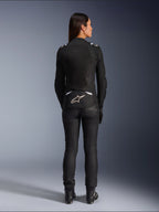 Veste Alpinestars Stella T-SPS Air v2, veste de moto textile pour femme, noir et blanc, vue de dos montrant les panneaux de ventilation en mesh et le logo blanc sur le bas du dos, portée avec un pantalon et des bottes de moto noirs, équipement de sport urbain.