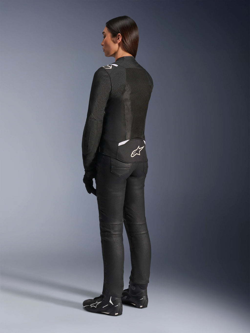 Veste Alpinestars Stella T-Sps Air V2, noir et blanc, vue de dos montrant les panneaux en mesh et le logo sur le bas du dos, associée à un pantalon de moto noir et des chaussures de moto, équipement de route sportif en textile pour femme