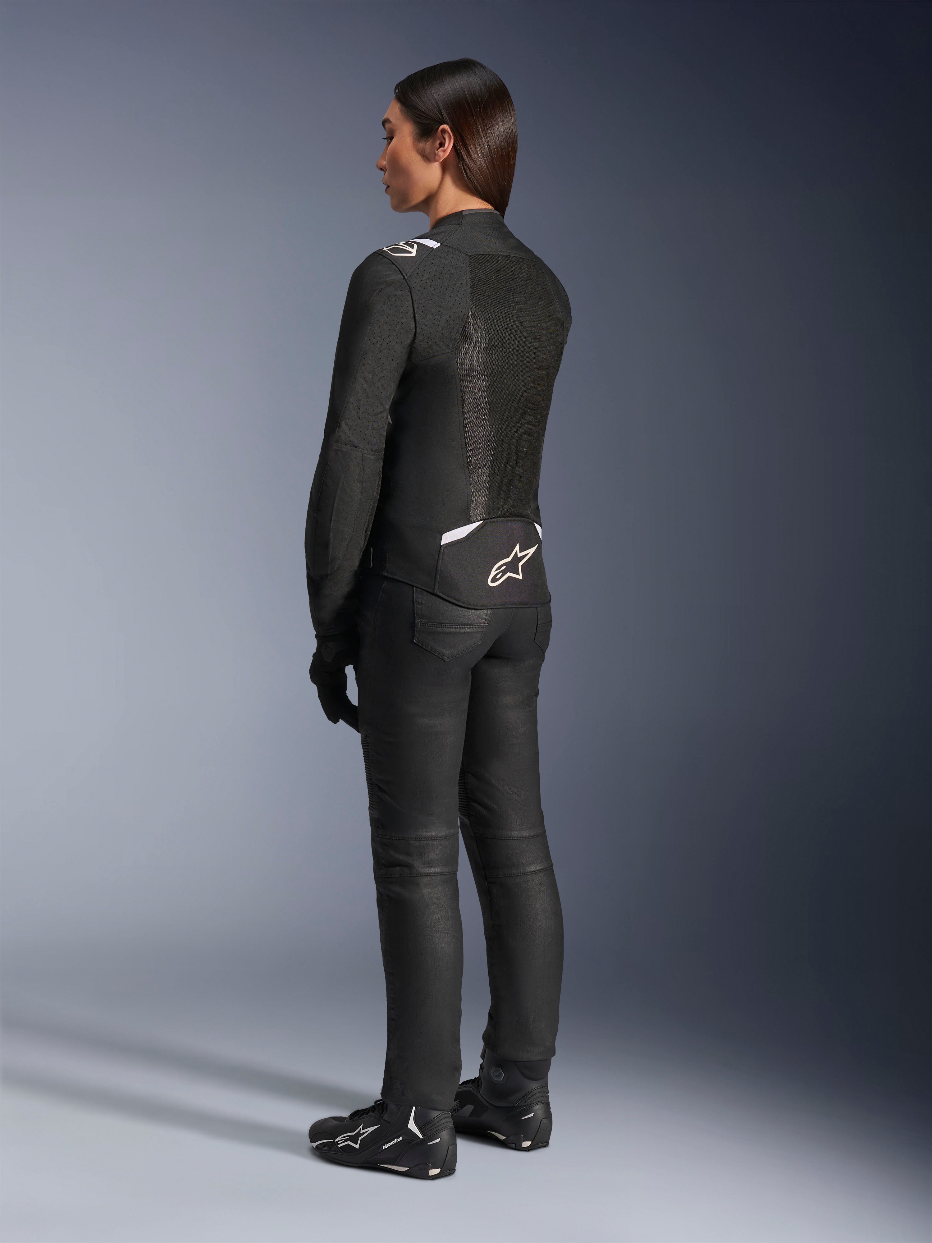 Veste Alpinestars Stella T-Sps Air V2, noir et blanc, vue de dos montrant les panneaux en mesh et le logo sur le bas du dos, associée à un pantalon de moto noir et des chaussures de moto, équipement de route sportif en textile pour femme