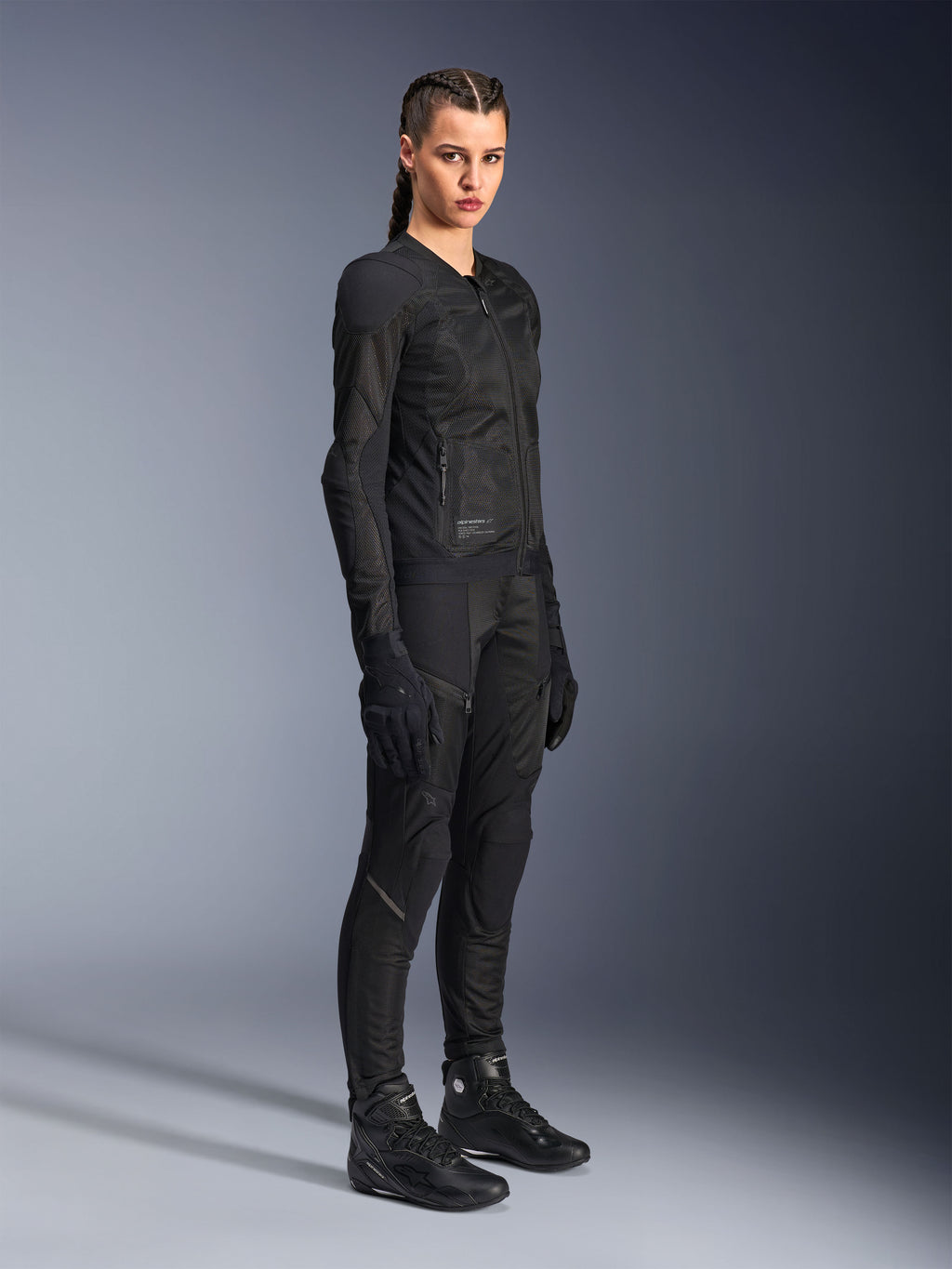 Motarde portant la veste Alpinestars Stella Troop-Air noire, dotée d'une construction technique en maille 2D, accompagnée d'un pantalon de moto, de gants et de bottes noirs assortis, conçue pour la conduite urbaine