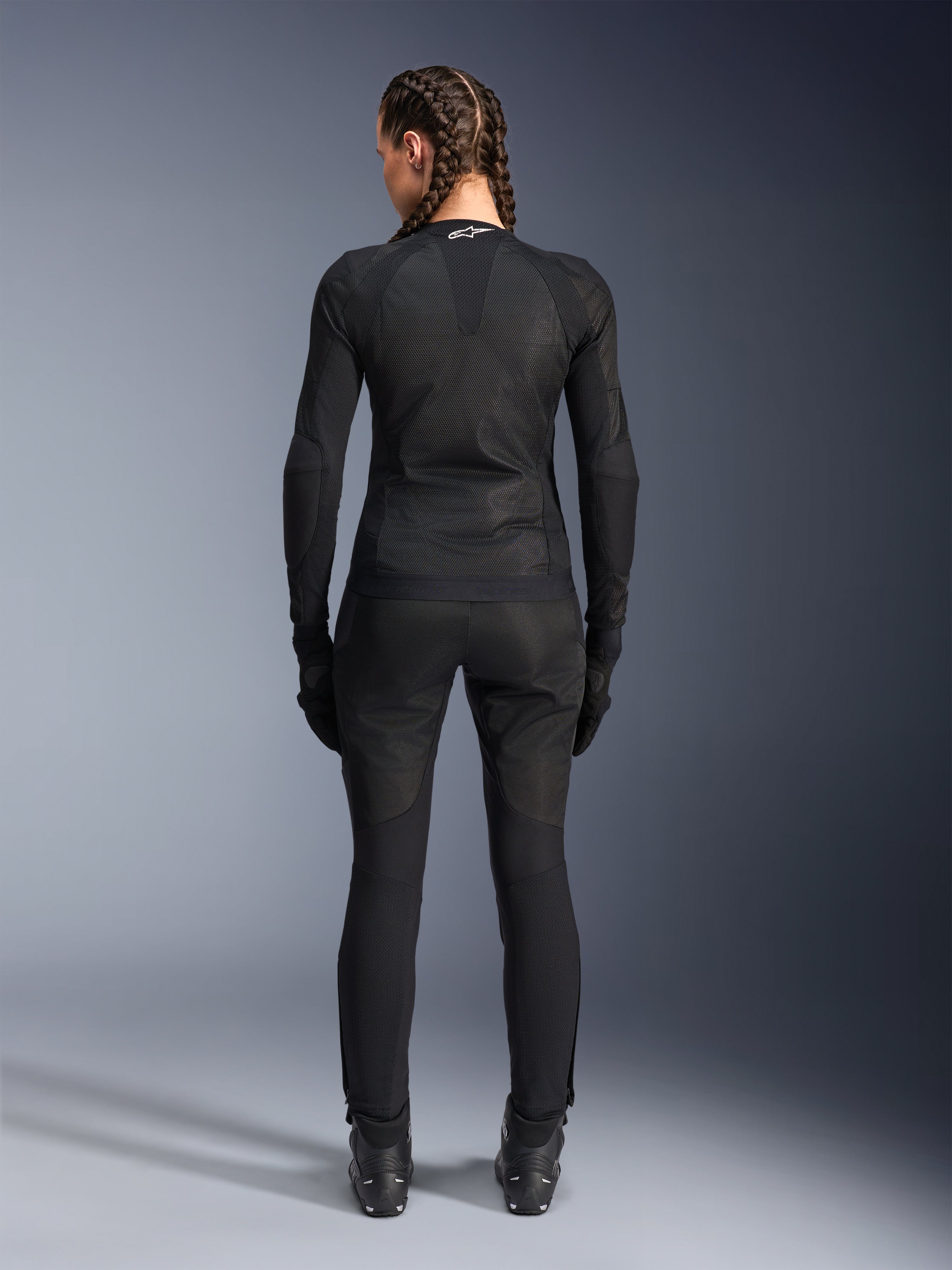 Veste Alpinestars Stella Troop-Air, veste de moto pour femme, noire, vue arrière d'une motarde portant une veste technique en maille, associée à un pantalon de moto, des gants et des bottes noirs assortis, coupe ajustée et respirante avec un logo Alpinestars blanc sur le col
