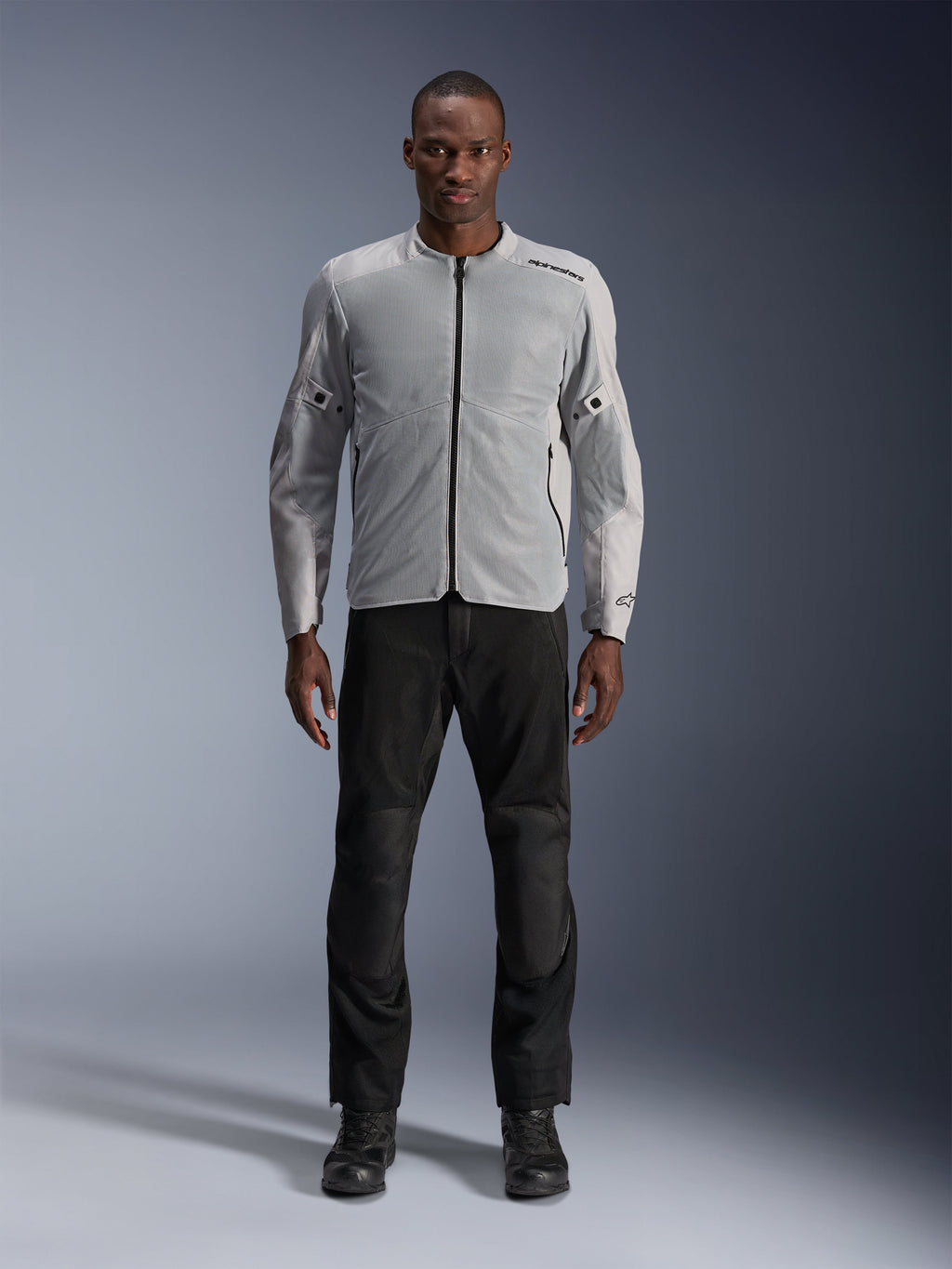 Veste Alpinestars C-1 Air en argent, veste de moto urbaine en textile pour homme avec panneaux en mesh aérés, portée par un mannequin avec un pantalon de moto noir et des bottes noires, style urbain contemporain