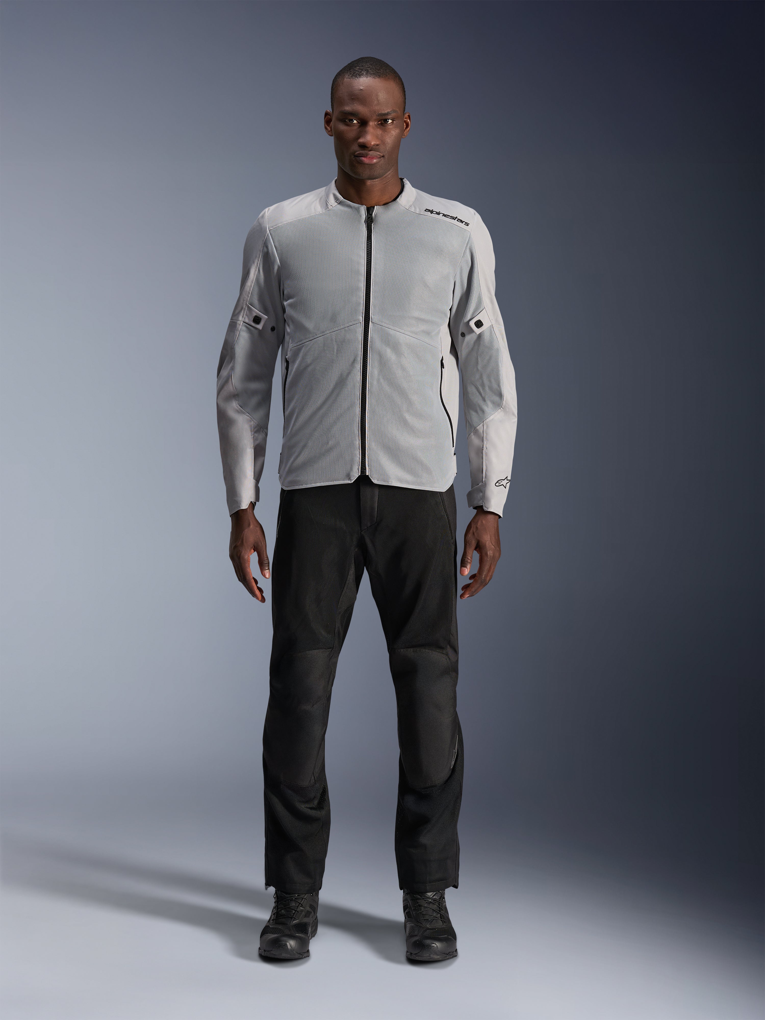Veste Alpinestars C-1 Air en argent, veste de moto urbaine en textile pour homme avec panneaux en mesh aérés, portée par un mannequin avec un pantalon de moto noir et des bottes noires, style urbain contemporain
