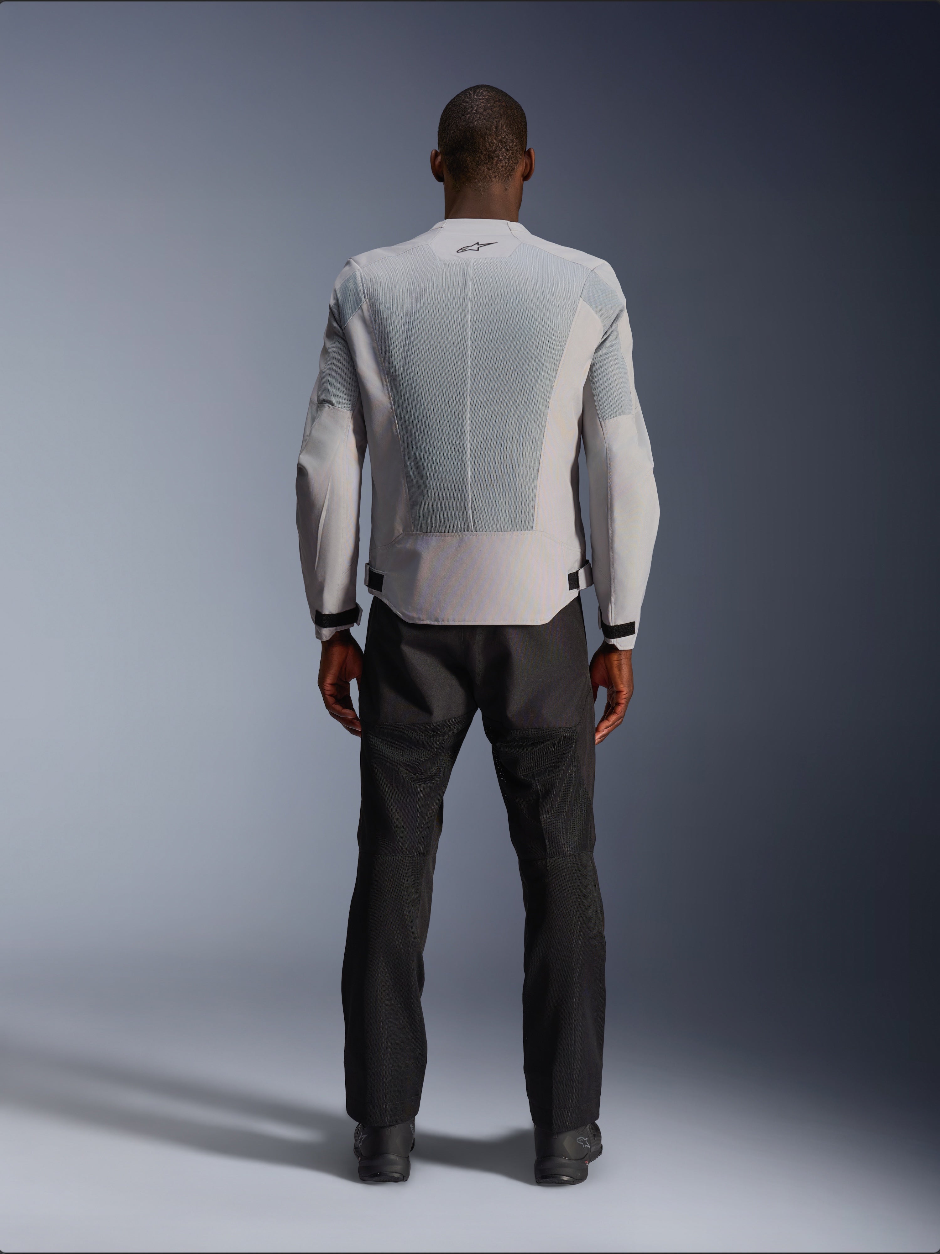 Veste Alpinestars C-1 Air en Silver, vue de dos sur un mannequin homme, veste de moto en textile dotée de larges panneaux de ventilation en maille technique, petit logo noir au niveau du col et ajusteurs de taille, portée avec un pantalon de moto noir pour un style urbain contemporain.