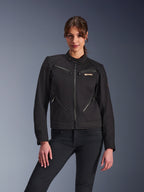 Veste Stella Grace Alpinestars pour femme, veste de moto urbaine, noire, vue de face, avec plusieurs poches zippées et un col à bouton-pression, portée avec un jean noir, équipement de protection moderne pour femme