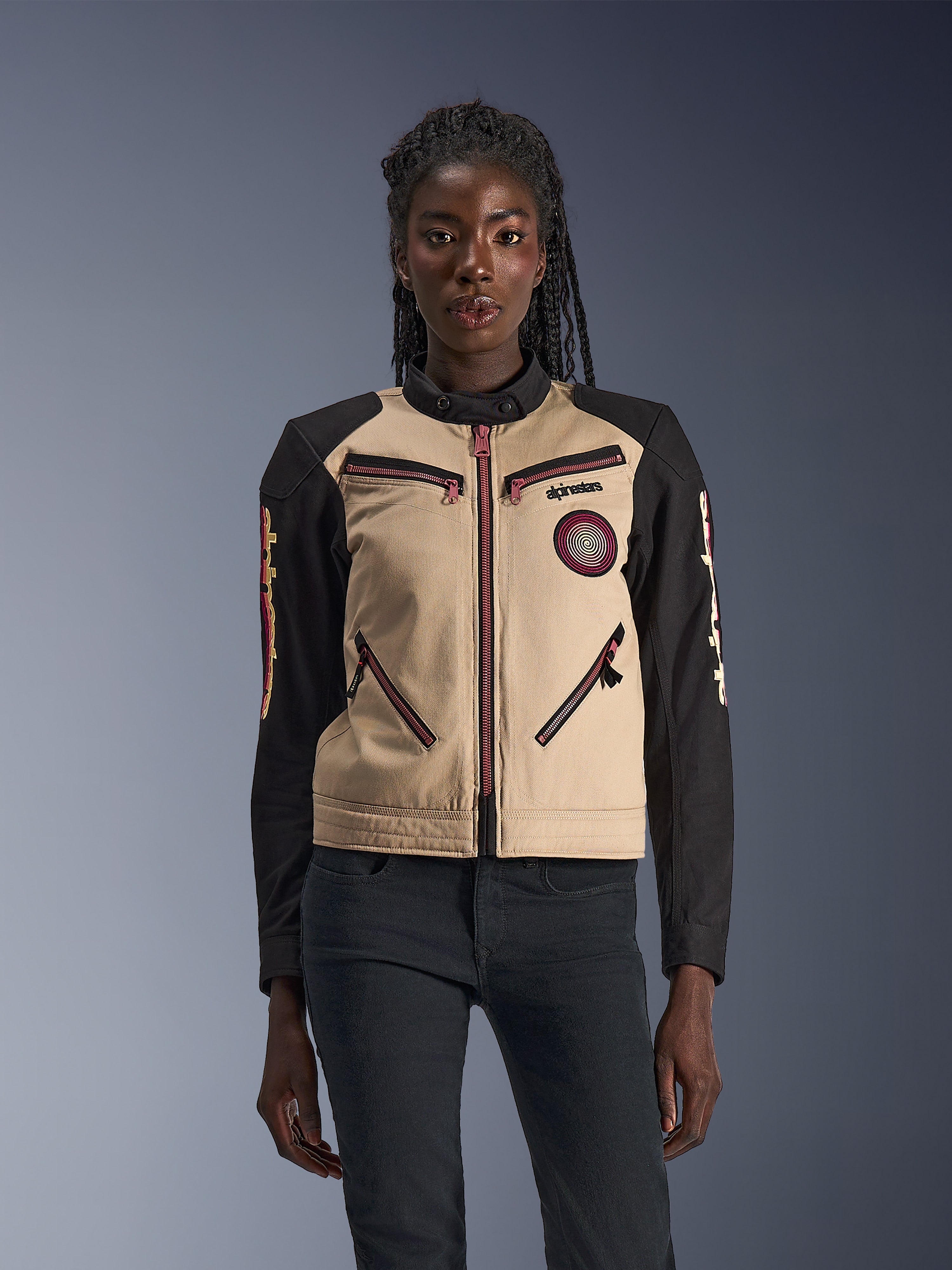 Veste Alpinestars Stella Grace, veste de moto pour femme, aluminium et noir, design d'inspiration workwear avec fermetures éclair rouge rosé, écusson en spirale sur la poitrine et manches noires avec motifs jaunes et rouges, portée par un mannequin