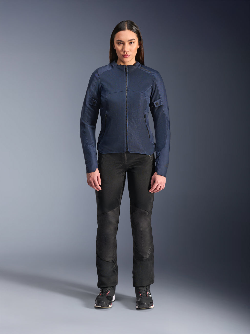 Modèle femme portant la veste Alpinestars Stella C-1 Air en bleu, veste de moto urbaine avec panneaux en maille technique, associée à un pantalon de moto noir et des baskets noires, vue de face en studio