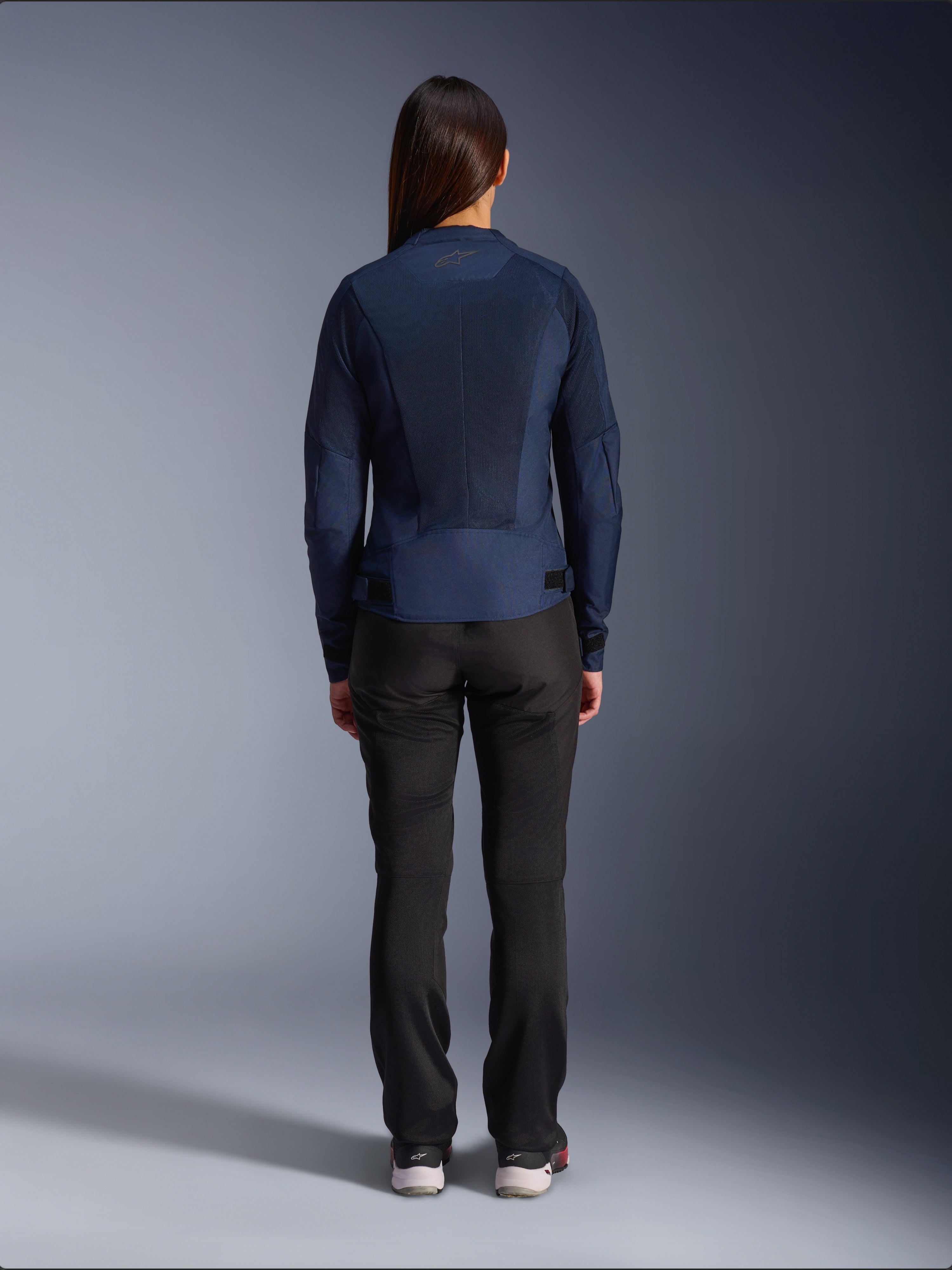 Veste Alpinestars Stella C-1 Air, veste de moto en textile pour femme, bleu marine, vue arrière présentant de larges panneaux en maille pour la ventilation et le logo Alpinestars sur le col, associée à un pantalon de moto noir pour un look urbain moderne
