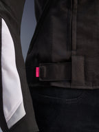 Alpinestars Stella T-GP Plus R V4 Jacket, Black and White, close-up of the adjustable waist strap with pink accent tab, durable textile construction with white sleeve paneling, sport-fit women's motorcycle jacket.