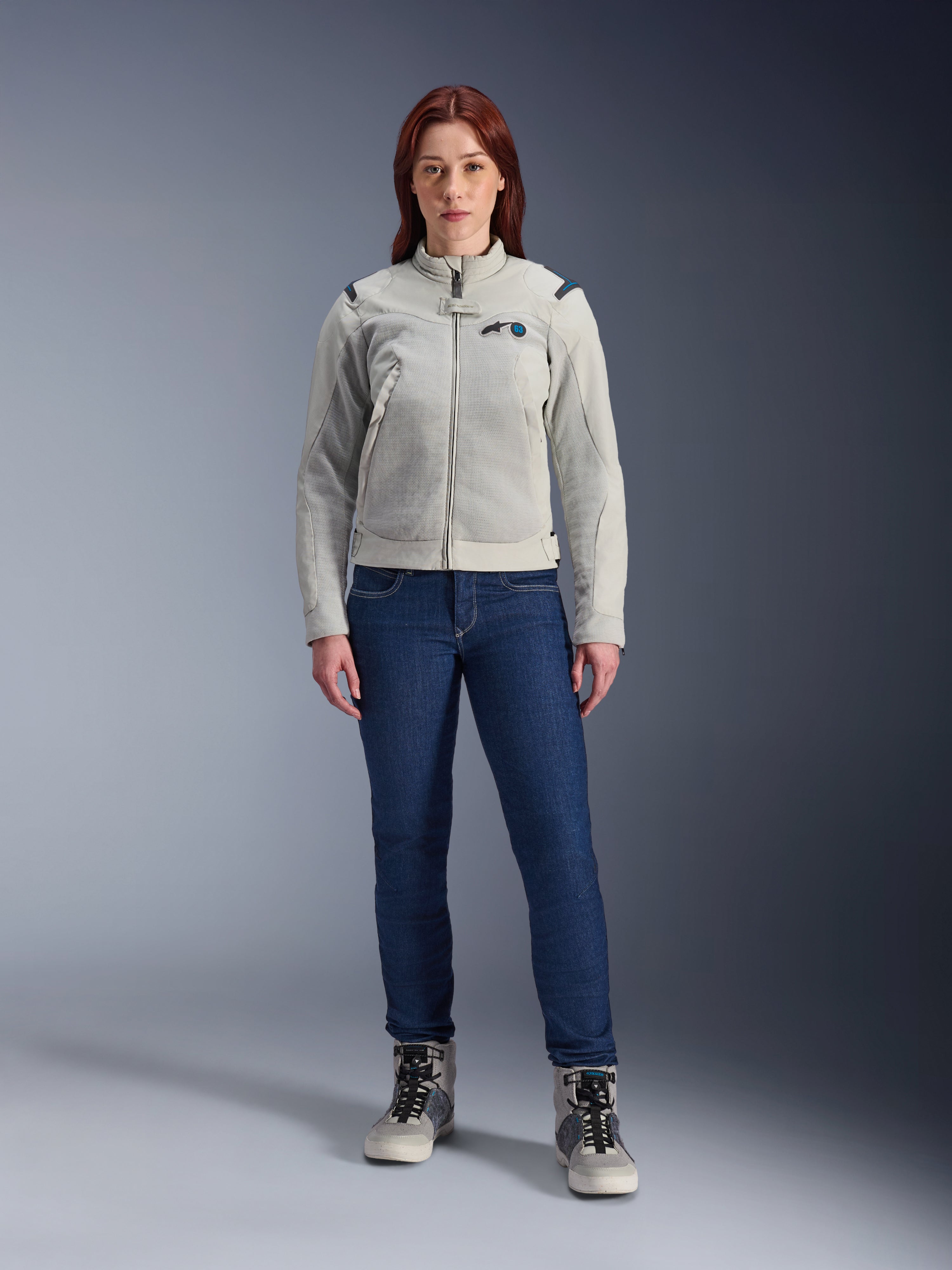 Veste Alpinestars Stella CIRCAL-1 Air, veste de moto pour femme, gris métal et bleu méthyle, portée avec un jean bleu foncé et des bottes de moto grises, dotée de panneaux en mesh pour la ventilation et d'un design urbain moderne