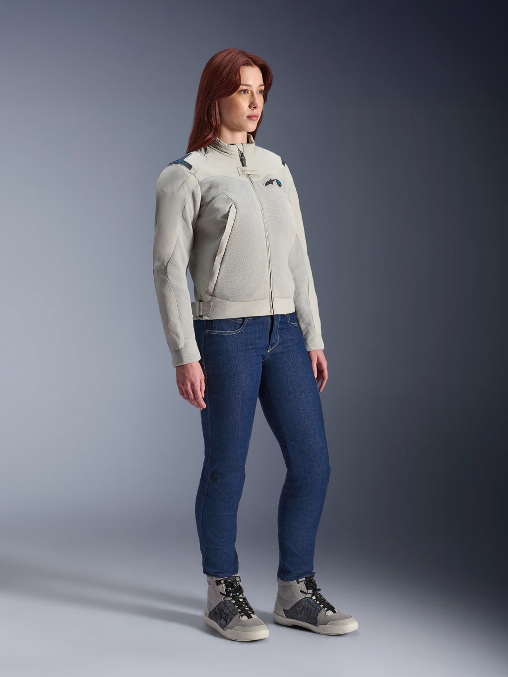 Femme portant la veste Alpinestars Stella Circal-1 Air en Metal Gray et Methyl Blue, associée à un jean bleu et des chaussures de moto décontractées, mettant en avant les panneaux en mesh et le design urbain minimaliste de la veste.