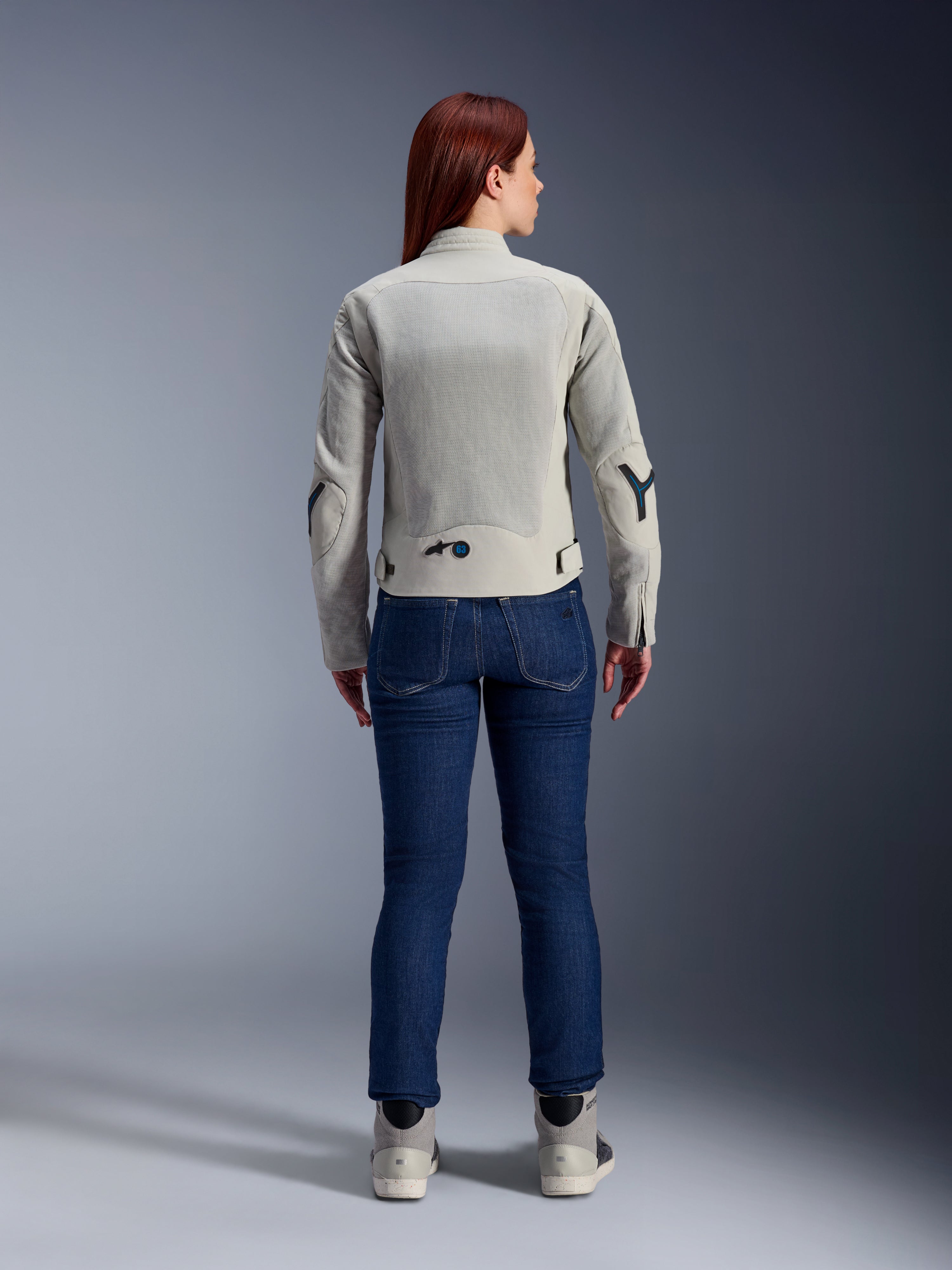 Veste Stella Circal-1 Air Femme Alpinestars en Metal Gray et Methyl Blue, vue de dos, avec de larges panneaux en mesh pour la circulation de l'air sur le dos et les bras, portée avec un jean en denim bleu foncé et des chaussures de moto grises pour un look urbain moderne.