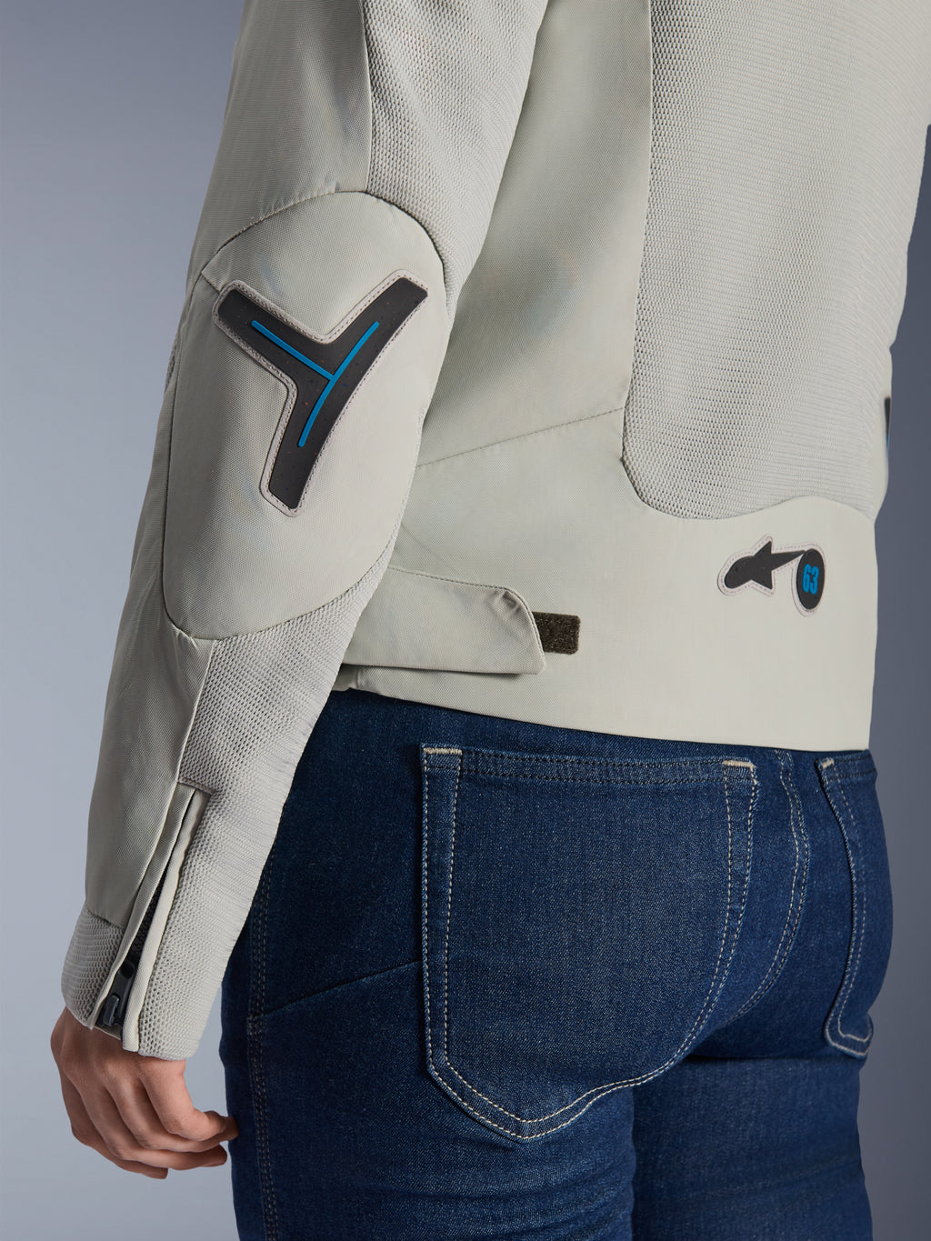 Veste Alpinestars Stella Circal-1 Air pour femme en gris métal et bleu méthyle, gros plan sur les détails du dos et de la manche montrant les panneaux de flux d'air en maille, les accents bleu néon sur le coude et la taille, et la patte de réglage, portée avec un jean en denim bleu foncé.