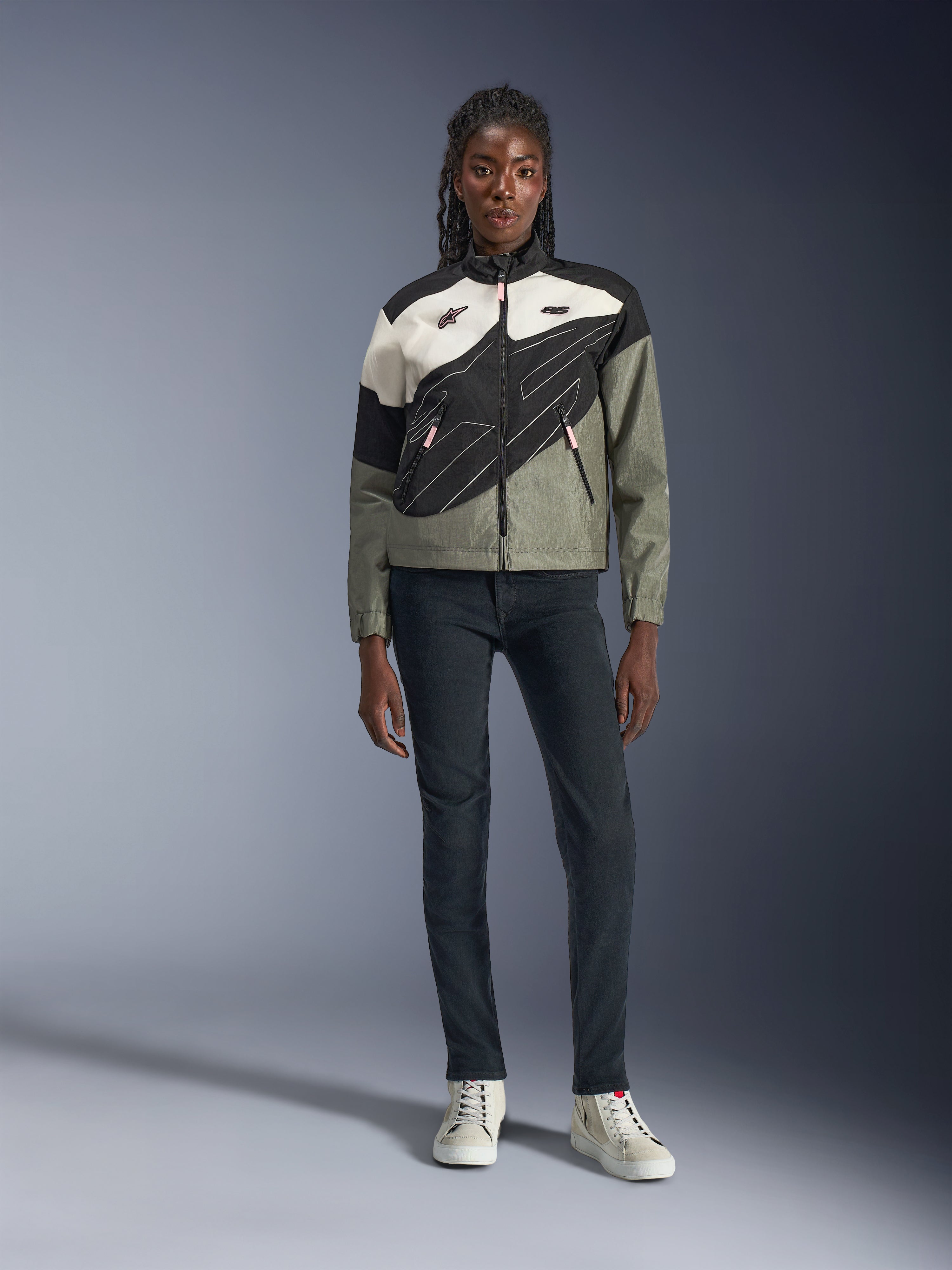 Alpinestars Stella Moshell Jacket, Women's Motorcycle Jacket, Black, Fur Gray, and Off White with Pink accents, worn by a model with dark jeans and off-white sneakers, featuring an asymmetrical zip-up design with bold geometric graphics, contemporary urban riding gear