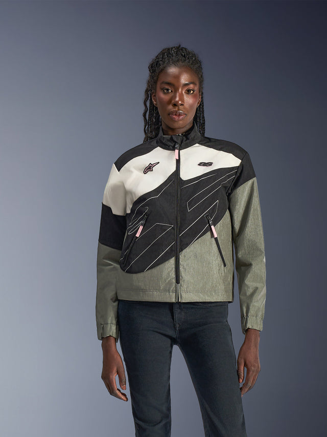 Femme portant la veste Alpinestars Stella Moshell, veste de moto urbaine en Noir, Gris, Blanc Cassé et Rose, design asymétrique avec graphismes techniques, tirettes roses et logos Alpinestars, style streetwear contemporain pour les motardes urbaines.