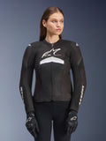 Alpinestars Stella T-GP Plus R V4 Airflow Jacket, veste de moto de course pour femme, noire avec des accents blancs et gris, conception en mesh texturé, logos sur la poitrine et les manches, portée avec des gants noirs et blancs assortis