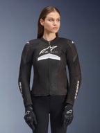 Alpinestars Stella T-GP Plus R V4 Airflow Jacket, veste de moto de course pour femme, noire avec des accents blancs et gris, conception en mesh texturé, logos sur la poitrine et les manches, portée avec des gants noirs et blancs assortis