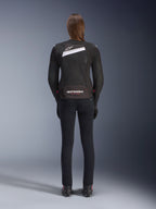 Veste Alpinestars Stella T-GP Plus R V4 Airflow, noir et blanc, vue de dos montrant les larges panneaux de ventilation en mesh et le logo Alpinestars, portée par une motarde avec un pantalon de moto noir coupe slim et des bottes, équipement textile de sport pour femme