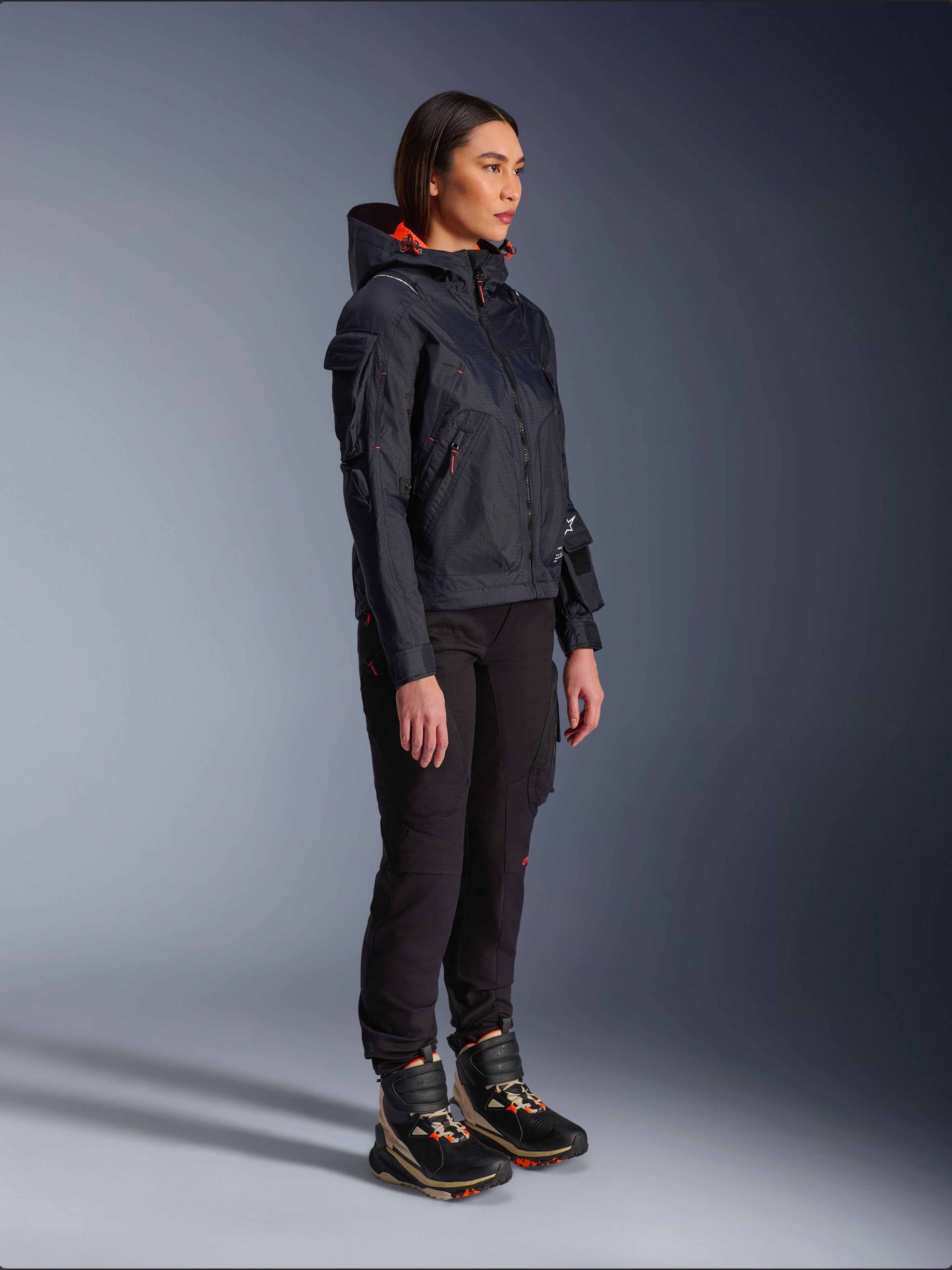 Pantalon femme Alpinestars Actea noir, coupe régulière avec poches cargo, associé à une veste Molly Air noire aux accents orange et des chaussures de moto montantes, vêtements de moto urbains contemporains pour femmes