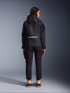 Pantalon Alpinestars Actea pour femme, pantalon de moto noir avec coupe fuselée, associé à une veste à capuche Molly Air foncée et des bottes beige, vue arrière d'une motarde en tenue de moto urbaine