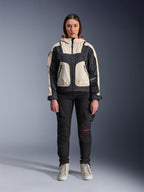 Mannequin femme portant la veste Alpinestars Molly Air en Black Almond, design color-block avec empiècements crème et noirs et capuche doublée de rouge, pantalon de moto noir et baskets crème, équipement de moto urbain contemporain, photo de studio
