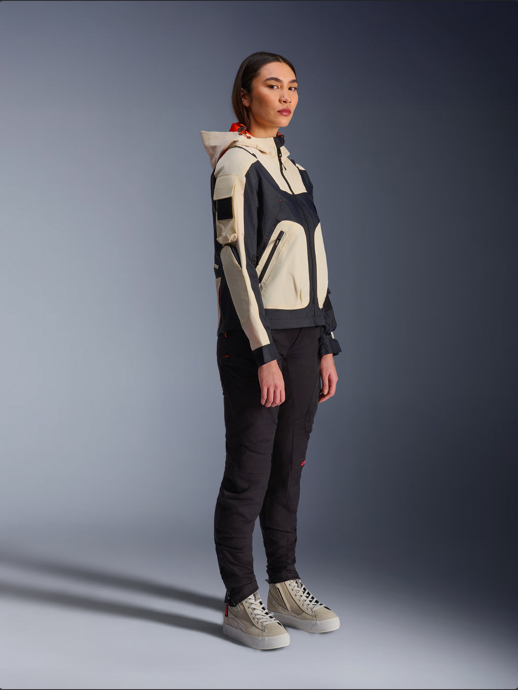 Veste Alpinestars Molly Air en Black Almond, portée par une motarde avec un pantalon noir et des baskets montantes crème, présentant un design bicolore avec des empiècements noirs et beige, une capuche intégrée et un style urbain contemporain.