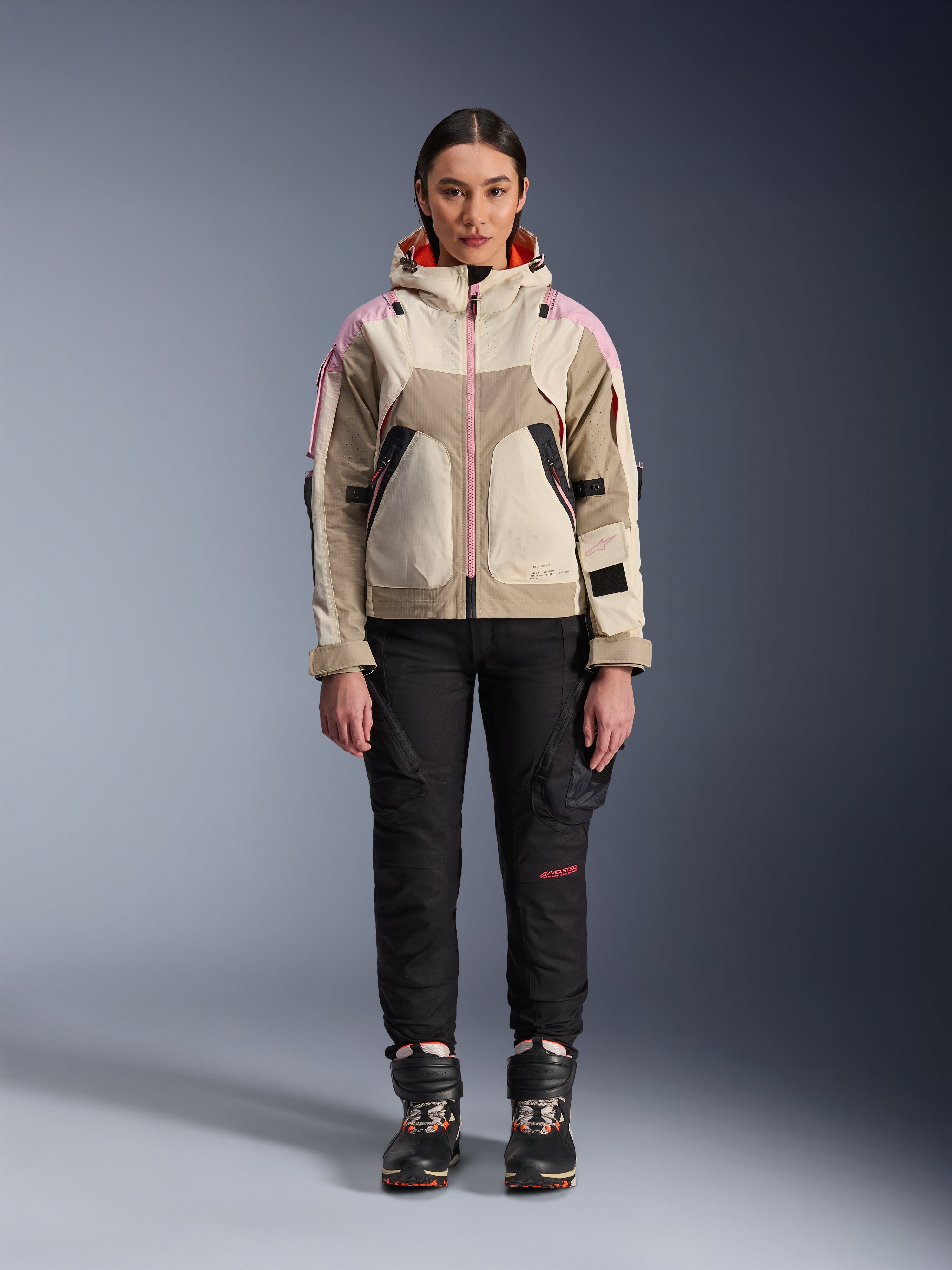 Mannequin femme portant la veste Alpinestars Molly Air en Sand Pink Almond, avec un pantalon de moto technique noir et des bottes, vue de face en pied, veste de moto urbaine au design d'inspiration utilitaire et accents roses