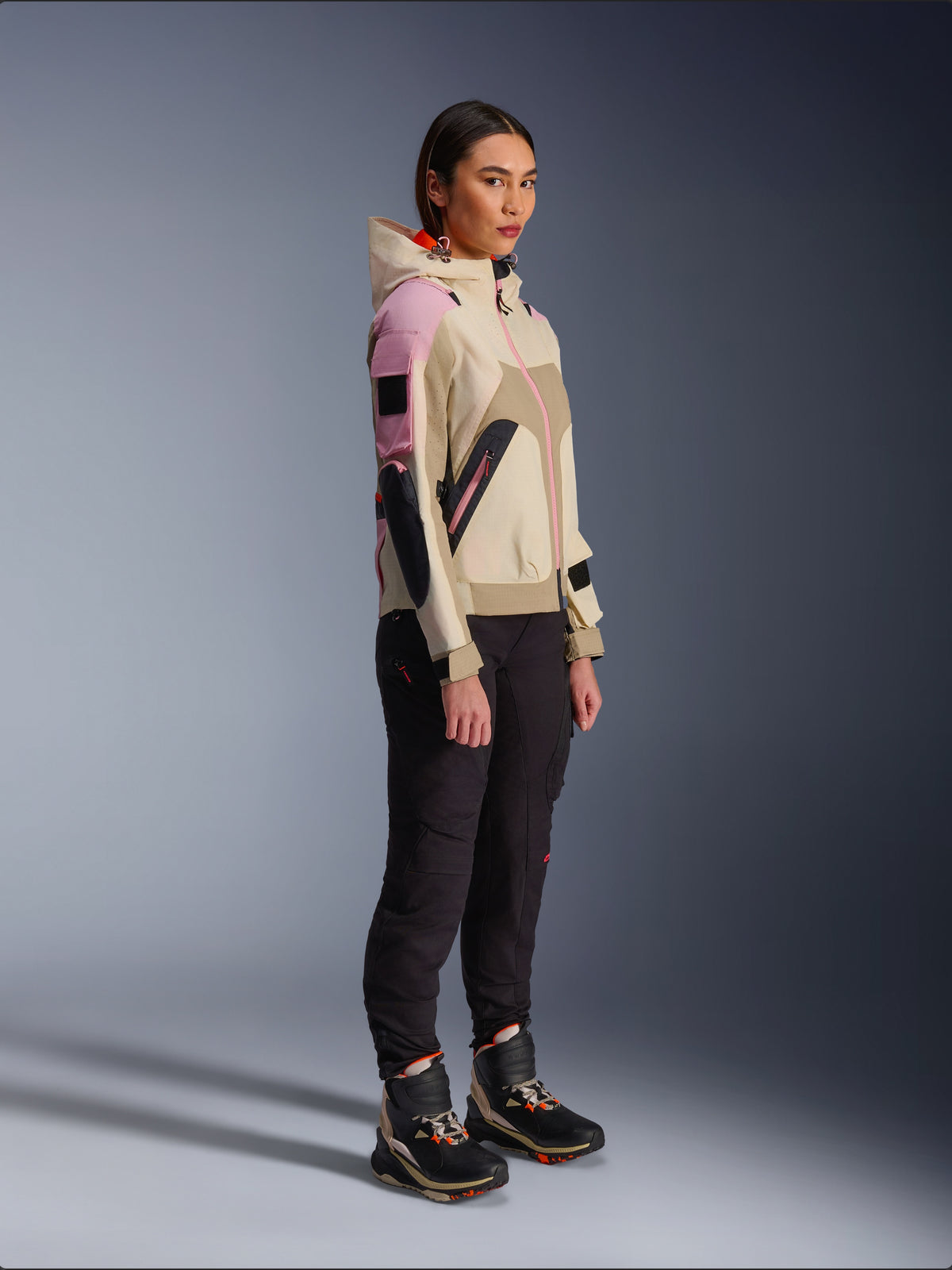 Mannequin femme portant la veste Alpinestars Molly Air en coloris Sand Pink Almond, associée à un pantalon technique sombre et des bottes de moto montantes, veste de moto urbaine avec capuche et empiècements multicolores, design contemporain inspiré du streetwear