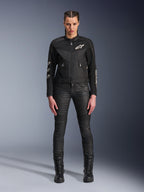 Modèle féminin portant la veste Alpinestars Stella T-Dyno Air, veste de moto noire pour femme avec panneaux en maille 3D et logos Astars blancs, accompagnée d'un pantalon de moto slim noir et de bottes à lacets noires, style d'équipement de conduite urbaine.