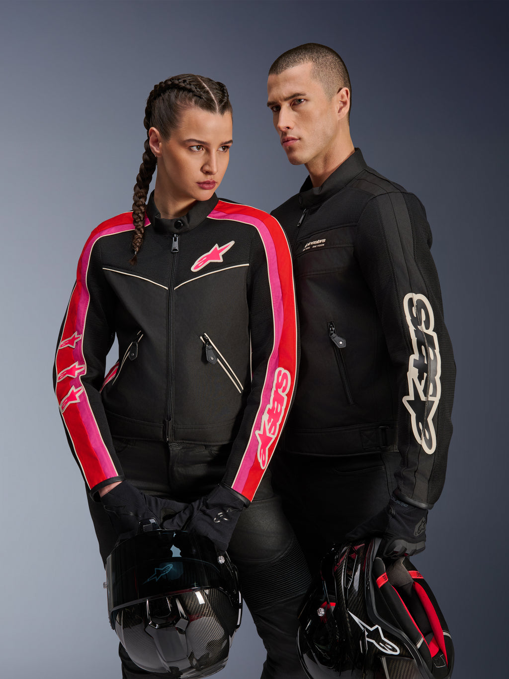 Veste Alpinestars Stella T-Dyno Air pour femme en coloris Noir Rouge Vif Fuchsia, associée à la veste Dyno Air noire pour homme, deux motards tenant des casques de moto, photo de studio d'équipement de moto urbain contemporain