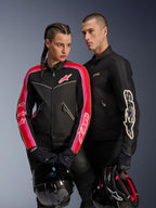 Veste Alpinestars Stella T-Dyno Air pour femme en coloris Noir Rouge Vif Fuchsia, associée à la veste Dyno Air noire pour homme, deux motards tenant des casques de moto, photo de studio d'équipement de moto urbain contemporain