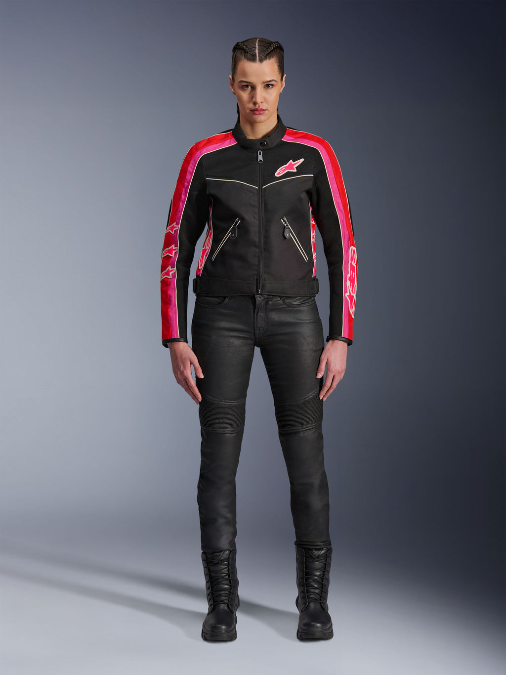 Motarde portant la veste Alpinestars Stella T-Dyno Air, noire avec des accents rouge vif et fuchsia, associée à un pantalon de moto noir et des bottes à lacets, avec panneaux en maille 3D, coupe ajustée et logos d'étoiles roses, tenue d'équipement de moto urbaine