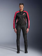 Motarde portant la veste Alpinestars Stella T-Dyno Air, noire avec des accents rouge vif et fuchsia, associée à un pantalon de moto noir et des bottes à lacets, avec panneaux en maille 3D, coupe ajustée et logos d'étoiles roses, tenue d'équipement de moto urbaine