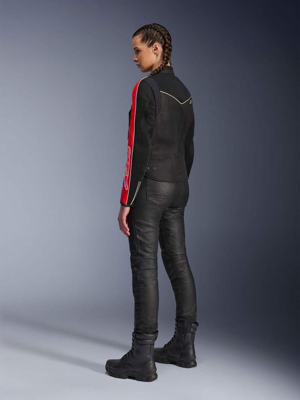 Femme portant la veste Alpinestars Stella T-Dyno Air en Noir Rouge Vif Fuchsia, associée à un pantalon de moto noir et des bottes noires, vue de profil mettant en valeur les graphismes rouges et fuchsia sur les manches et la coupe biker ajustée.