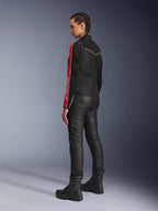 Femme portant la veste Alpinestars Stella T-Dyno Air en Noir Rouge Vif Fuchsia, associée à un pantalon de moto noir et des bottes noires, vue de profil mettant en valeur les graphismes rouges et fuchsia sur les manches et la coupe biker ajustée.