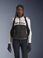 Veste Alpinestars Stella SMX Air pour femme, Ice Gray, Noir et Corail Fluo, construction en mesh et panneaux perforés, portée par un mannequin avec gants et pantalon de moto noirs, vue de face.