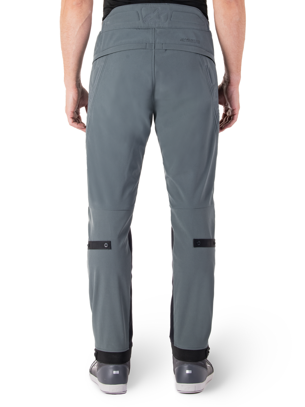 Pantalon Alpinestars Alden, Urban Gray, vue arrière d'un pantalon de moto urbain pour homme, coupe ajustée sous le genou avec des sangles de réglage noires aux mollets, design à taille haute arborant le mot-symbole MO.ST.EQ. sur l'empiècement arrière, porté avec des chaussures de moto grises