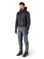 Pantalon Alpinestars Alden en Gris Urbain, porté par un mannequin avec une veste noire à capuche matelassée, des gants et des chaussures de moto, présentant des détails matelassés sur les côtés et des panneaux noirs à l'intérieur des jambes, équipement de moto urbain inspiré du streetwear.