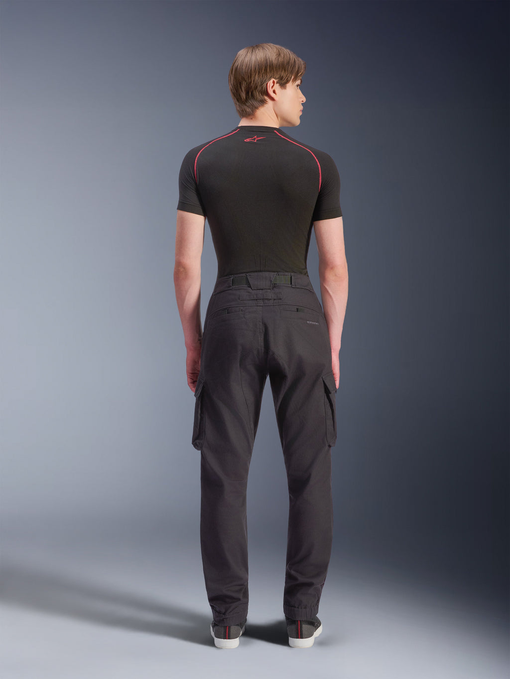 Alpinestars Flex-AST Cargo Pants - Short, noir, pantalon de moto urbain vu de dos, doté de poches cargo latérales et d'ourlets élastiqués, porté avec une couche de base noire à manches courtes aux surpiqûres rouges contrastées