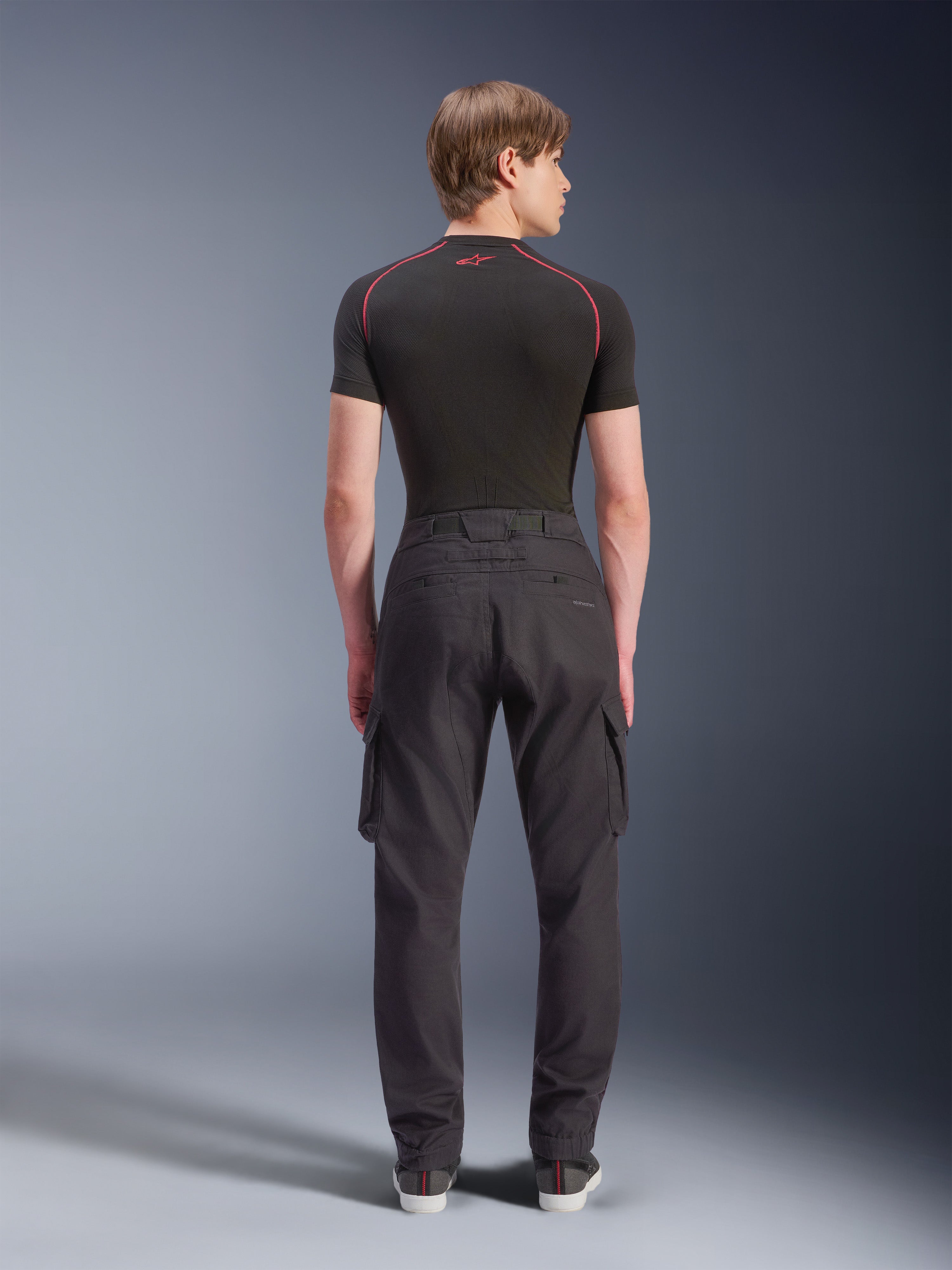 Alpinestars Flex-AST Cargo Pants - Short, noir, pantalon de moto urbain vu de dos, doté de poches cargo latérales et d'ourlets élastiqués, porté avec une couche de base noire à manches courtes aux surpiqûres rouges contrastées